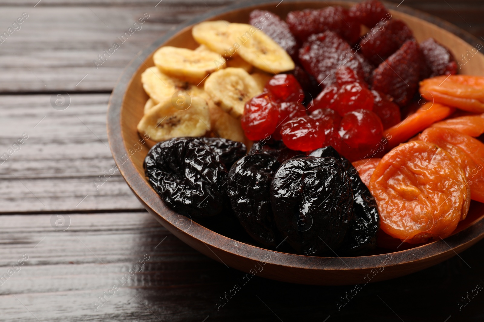 Photo of Mix of delicious dried fruits in bowl on wooden table, closeup