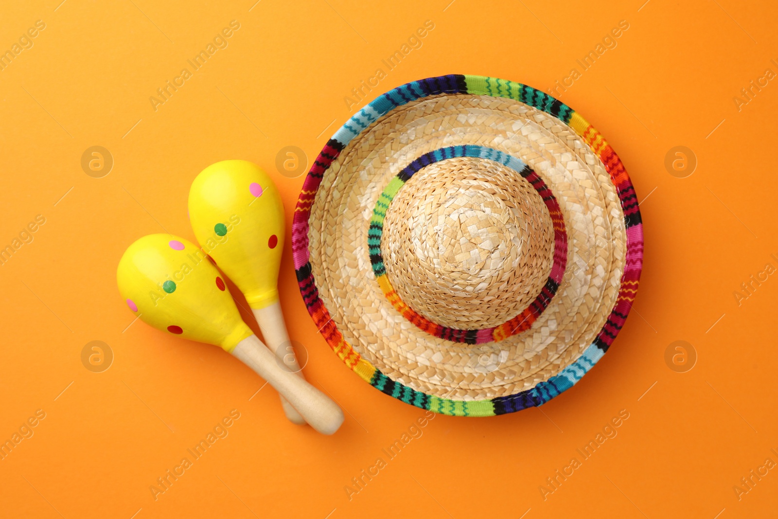 Photo of Mexican sombrero hat and maracas on orange background, flat lay