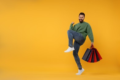 Photo of Excited man with many paper shopping bags on orange background. Space for text