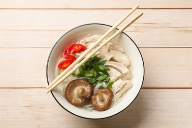 Photo of Delicious ramen with meat in bowl and chopsticks on wooden table, top view. Noodle soup