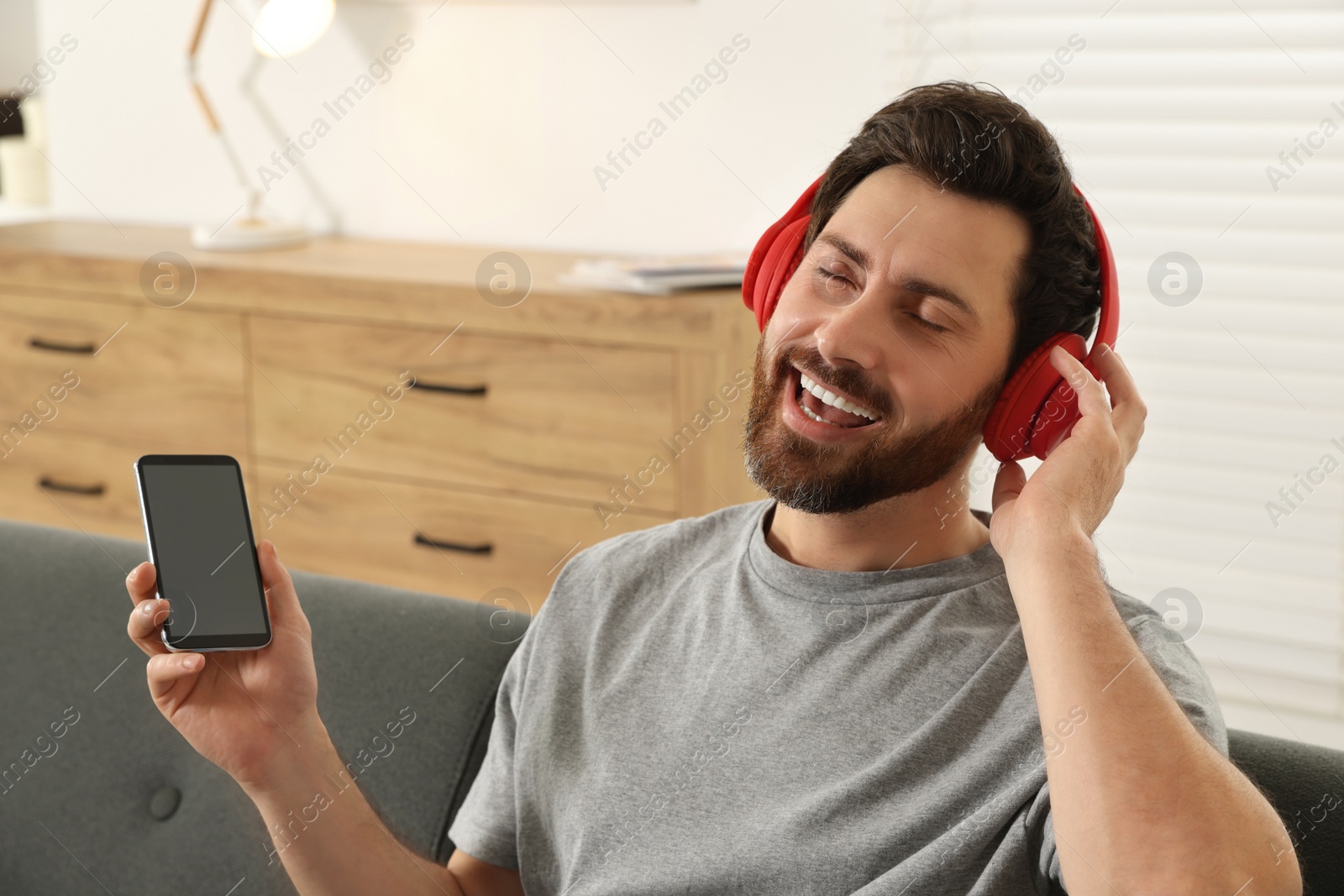 Photo of Happy man listening music with headphones on sofa indoors