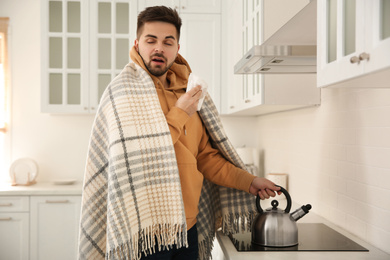 Photo of Sick young man putting heating kettle in kitchen. Influenza virus