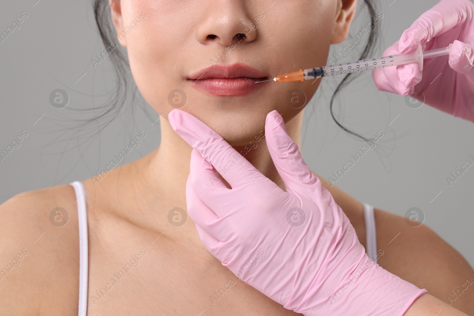 Photo of Woman getting lip injection on grey background, closeup