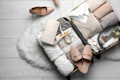 Photo of Open suitcase with folded clothes, shoes and accessories on floor, top view