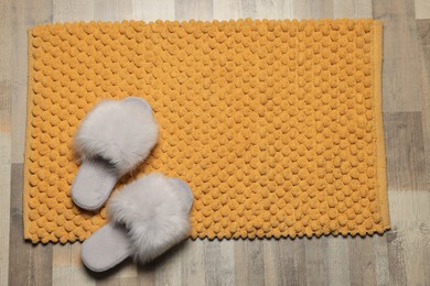 Photo of Soft orange bath mat and slippers on floor, top view