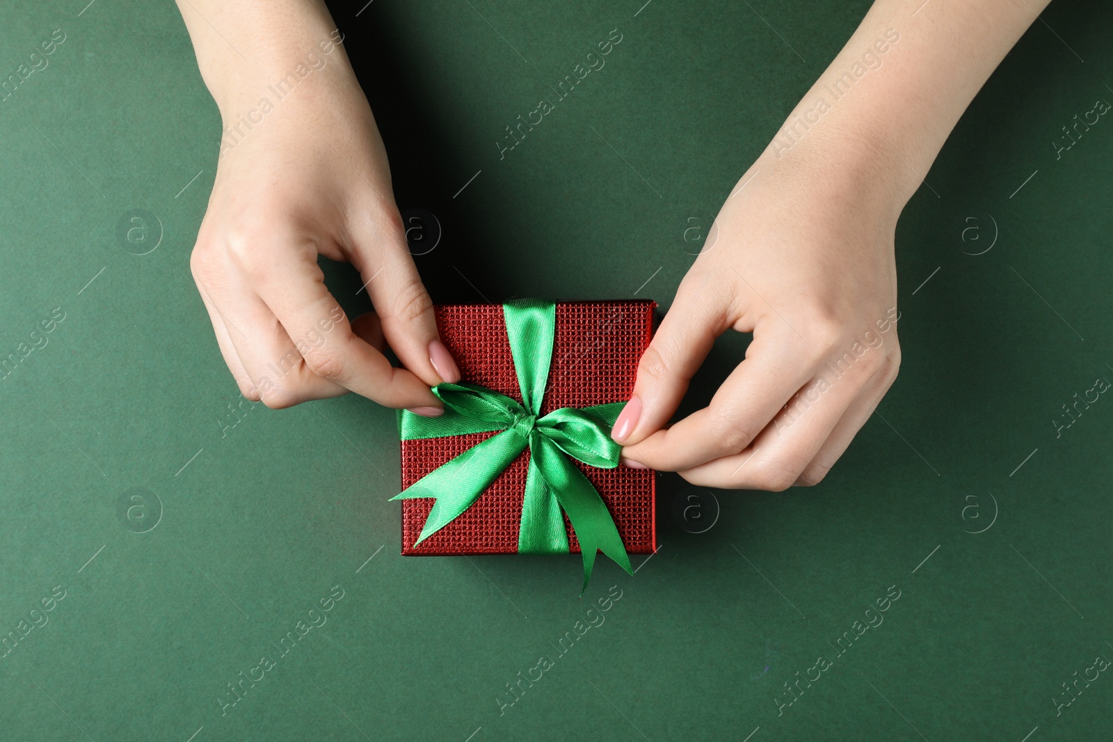 Photo of Woman decorating gift box on dark green background, top view. Christmas present