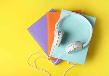 Modern headphones with hardcover books on color background, top view