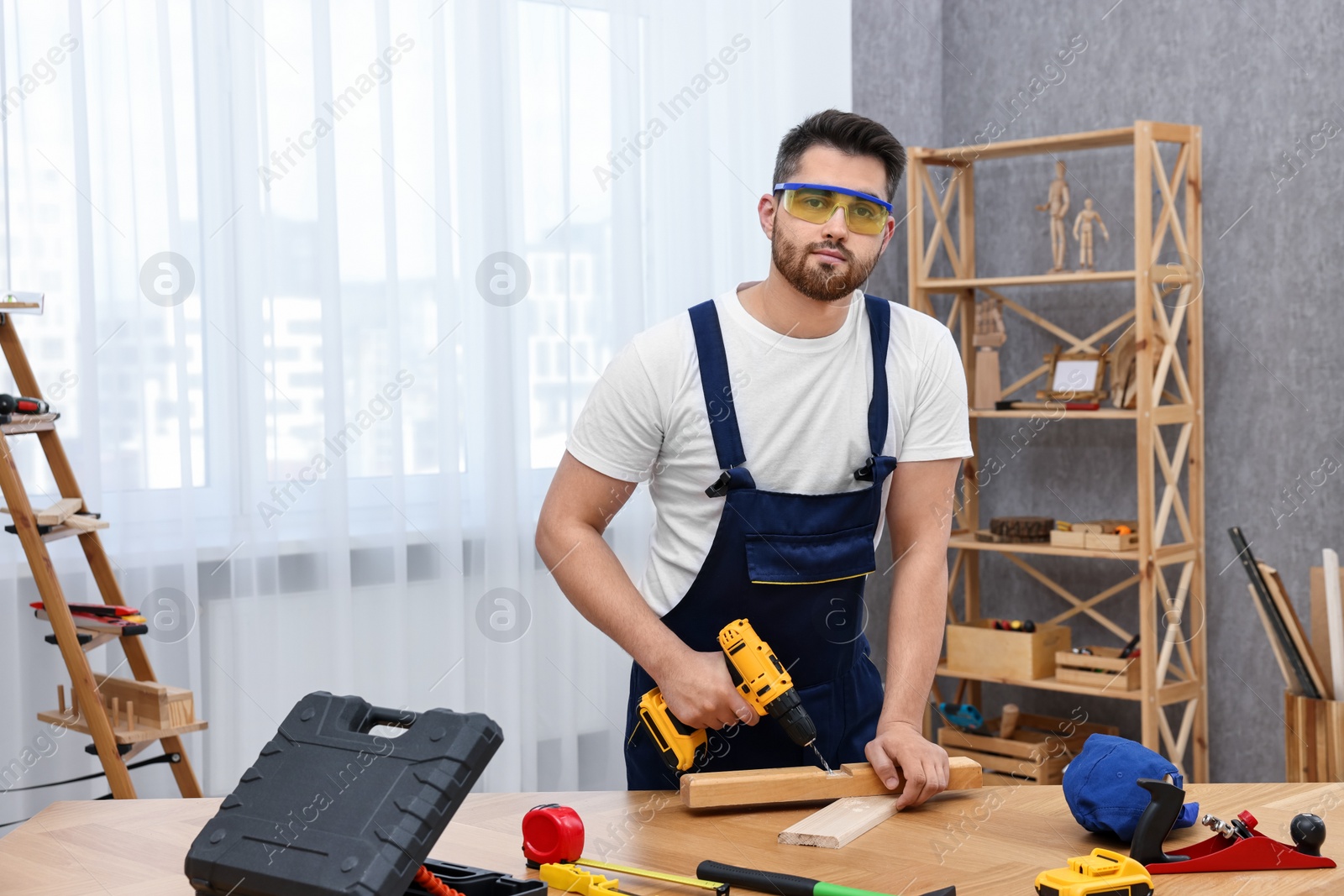 Photo of Young worker using electric drill at table in workshop