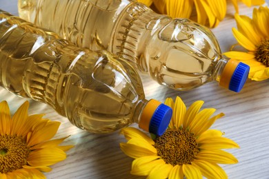 Photo of Bottles of sunflower oil and flowers on light wooden table