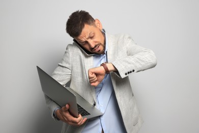 Photo of Emotional man with laptop checking time while talking on phone against grey background. Being late concept