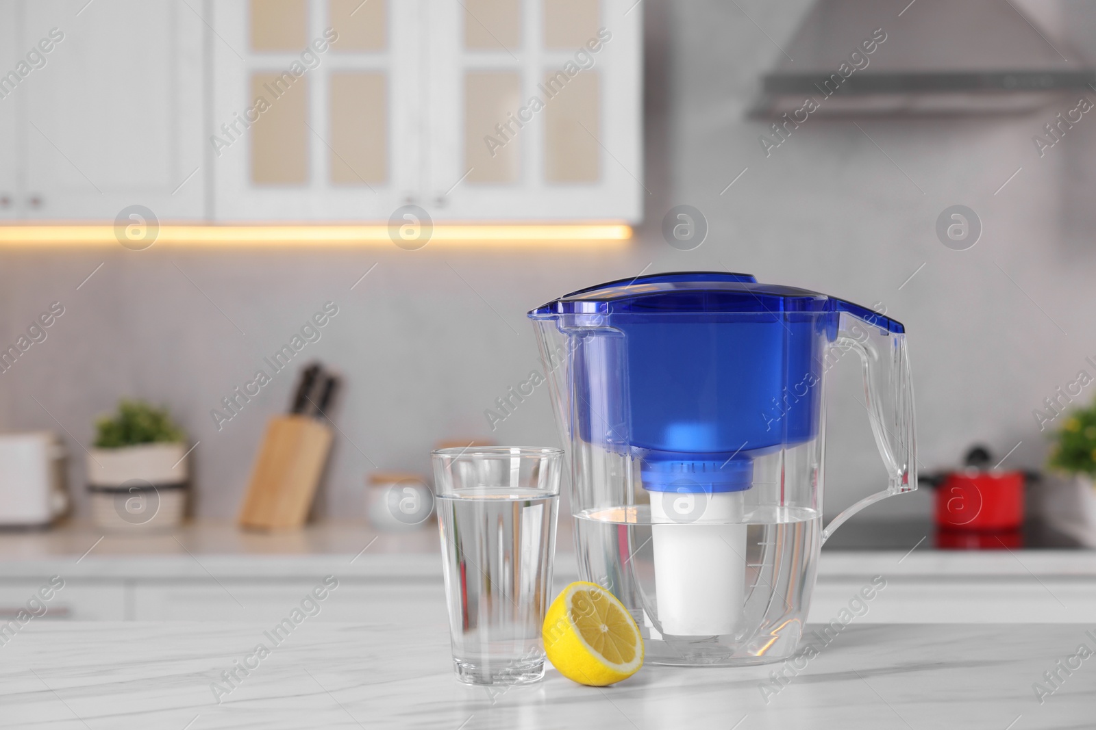 Photo of Water filter jug, glass and lemon on white marble table in kitchen, closeup. Space for text