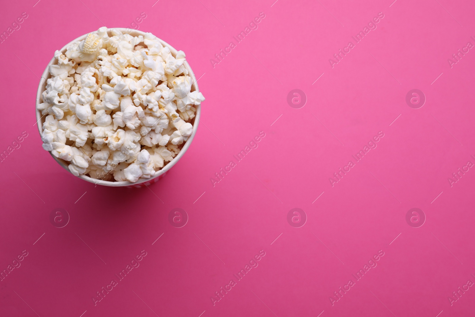 Photo of Paper bucket with delicious popcorn on pink background, top view. Space for text