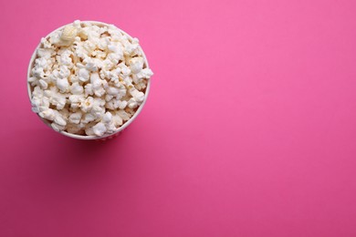 Photo of Paper bucket with delicious popcorn on pink background, top view. Space for text