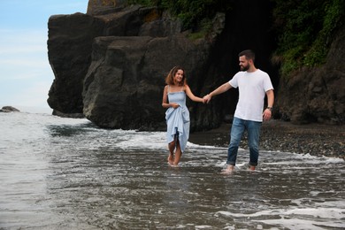 Happy young couple walking on beach near sea. Space for text