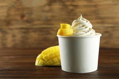 Cup of tasty frozen yogurt with mango on wooden table. Space for text