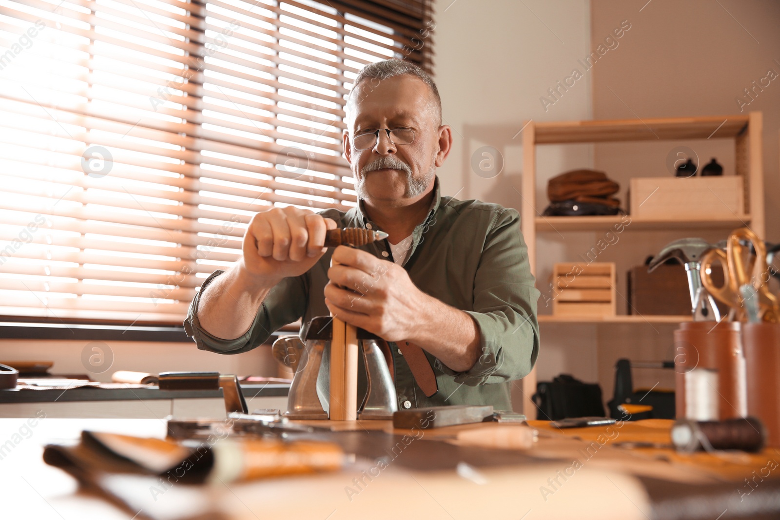 Photo of Man burnishing edges of leather belt in workshop