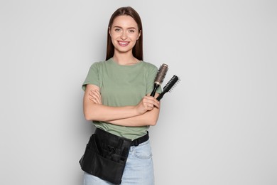 Portrait of happy hairdresser with brushes on light background