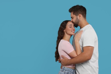 Man kissing his smiling girlfriend on light blue background. Space for text