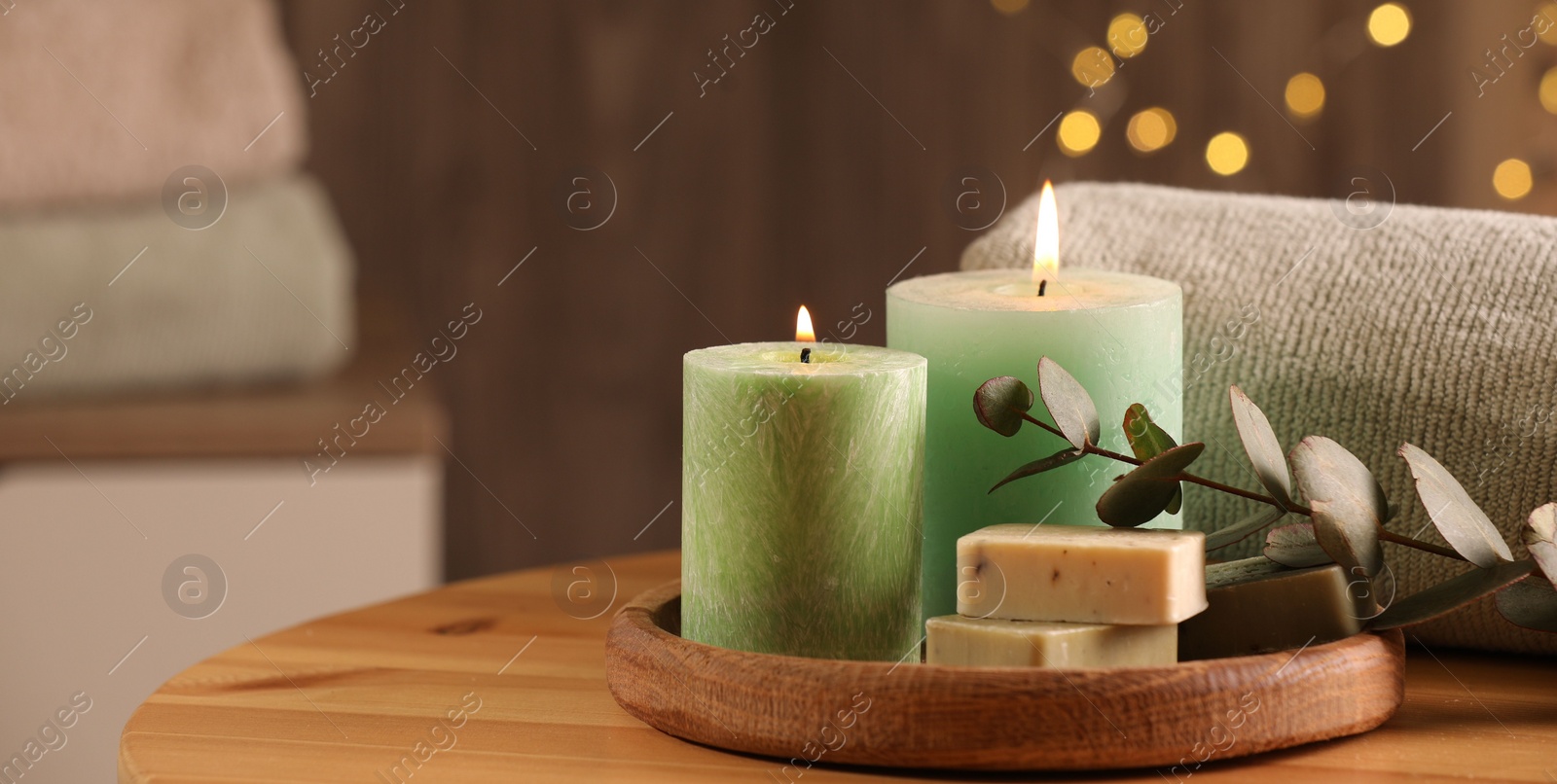 Photo of Spa composition. Burning candles, soap, towel and eucalyptus branch on wooden table, space for text