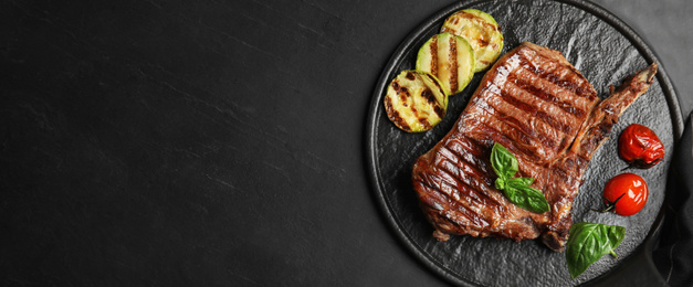 Image of Slate plate with grilled meat steak and space for text on black table, top view. Banner design