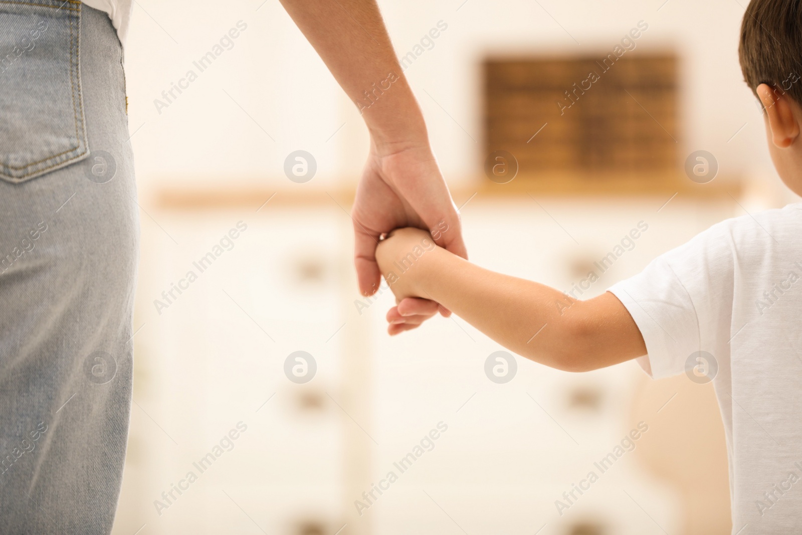 Photo of Mother holding hands with her child indoors, closeup. Happy family