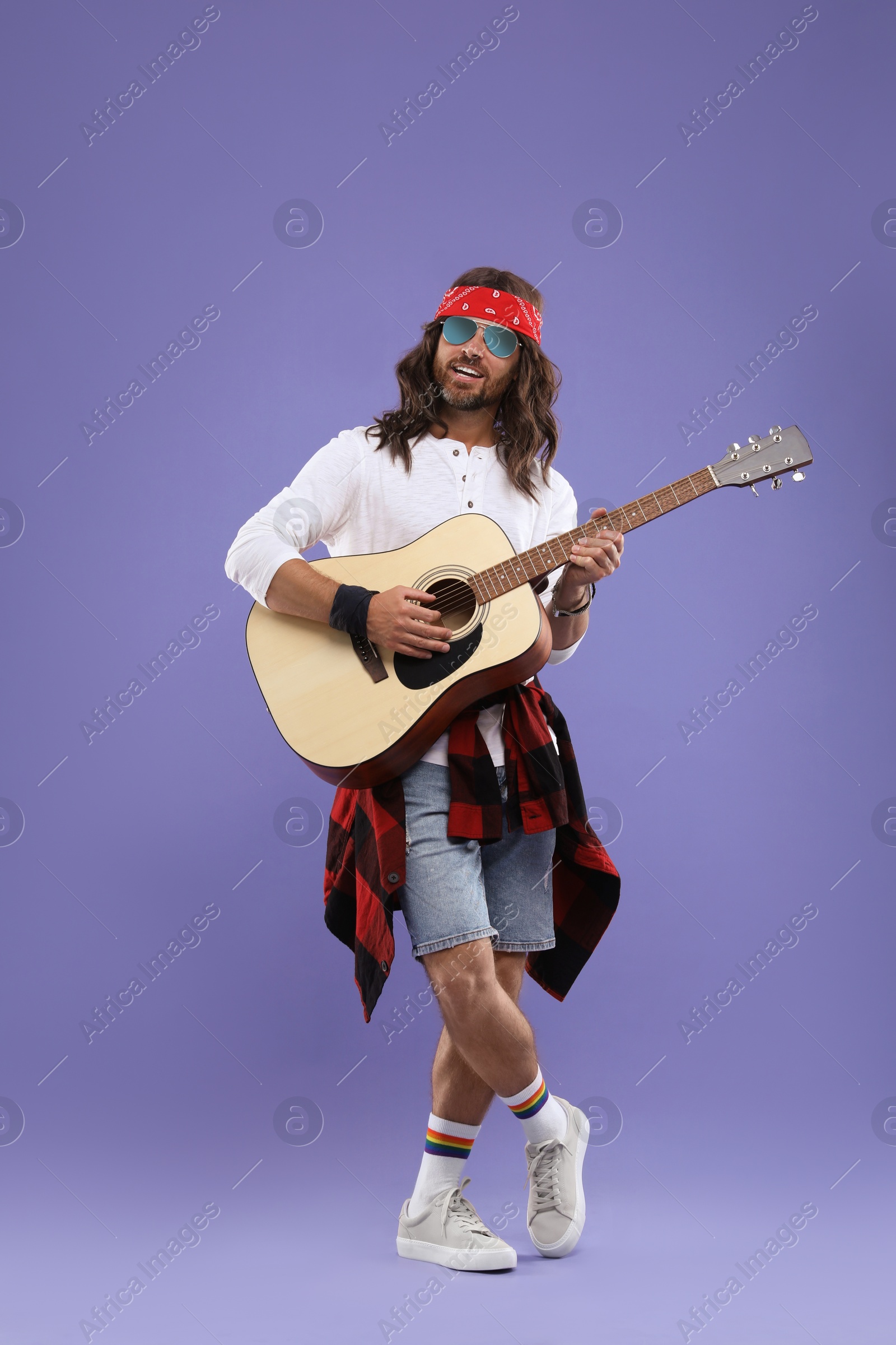 Photo of Stylish hippie man in sunglasses playing guitar on violet background