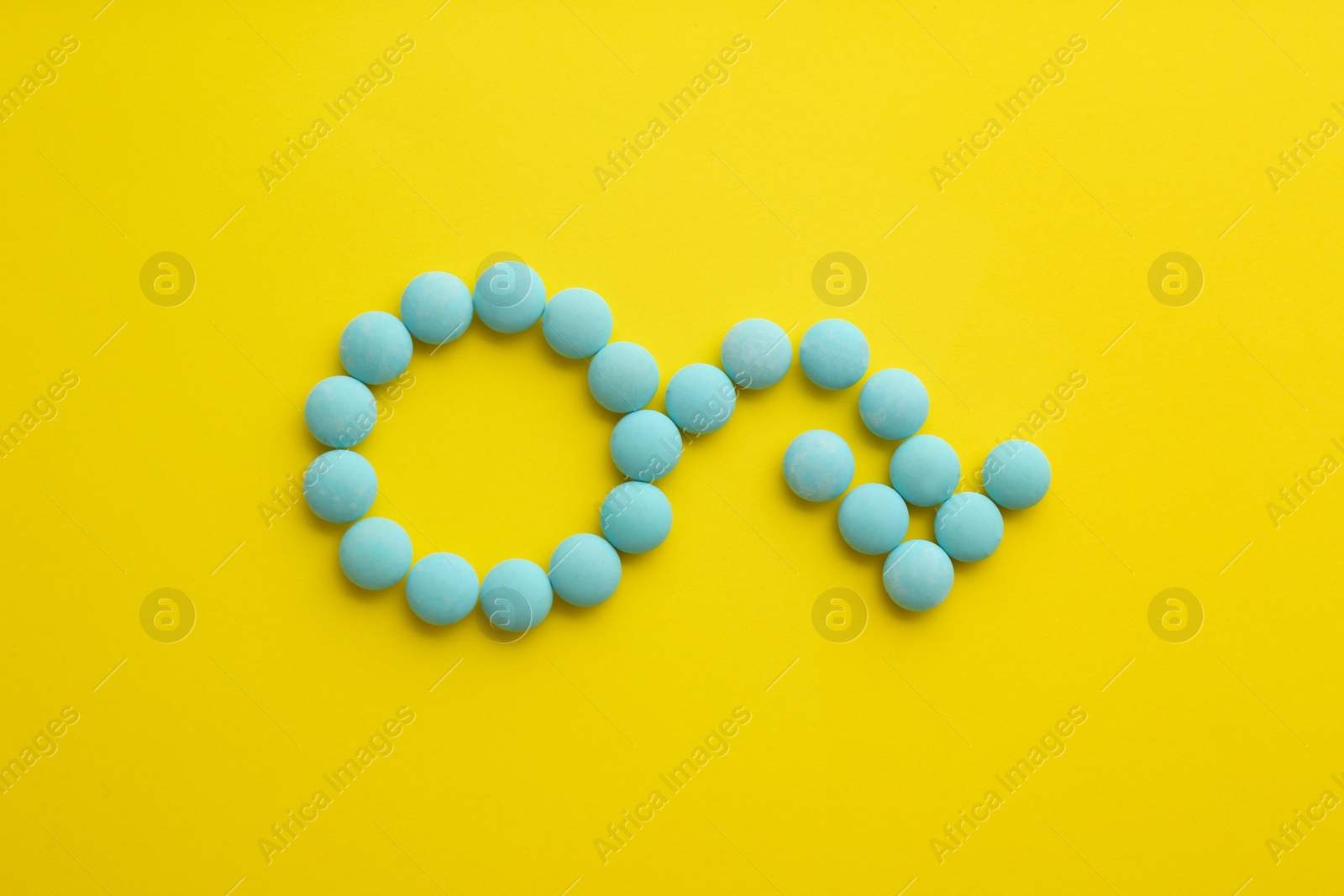 Photo of Male sign with bent arrow of blue pills symbolizing potency problems on yellow background, flat lay