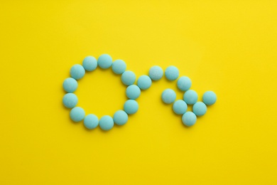 Male sign with bent arrow of blue pills symbolizing potency problems on yellow background, flat lay