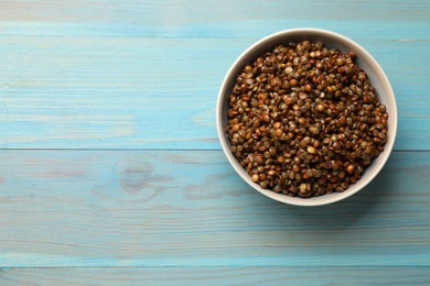 Photo of Delicious lentils in bowl on light blue wooden table, top view. Space for text