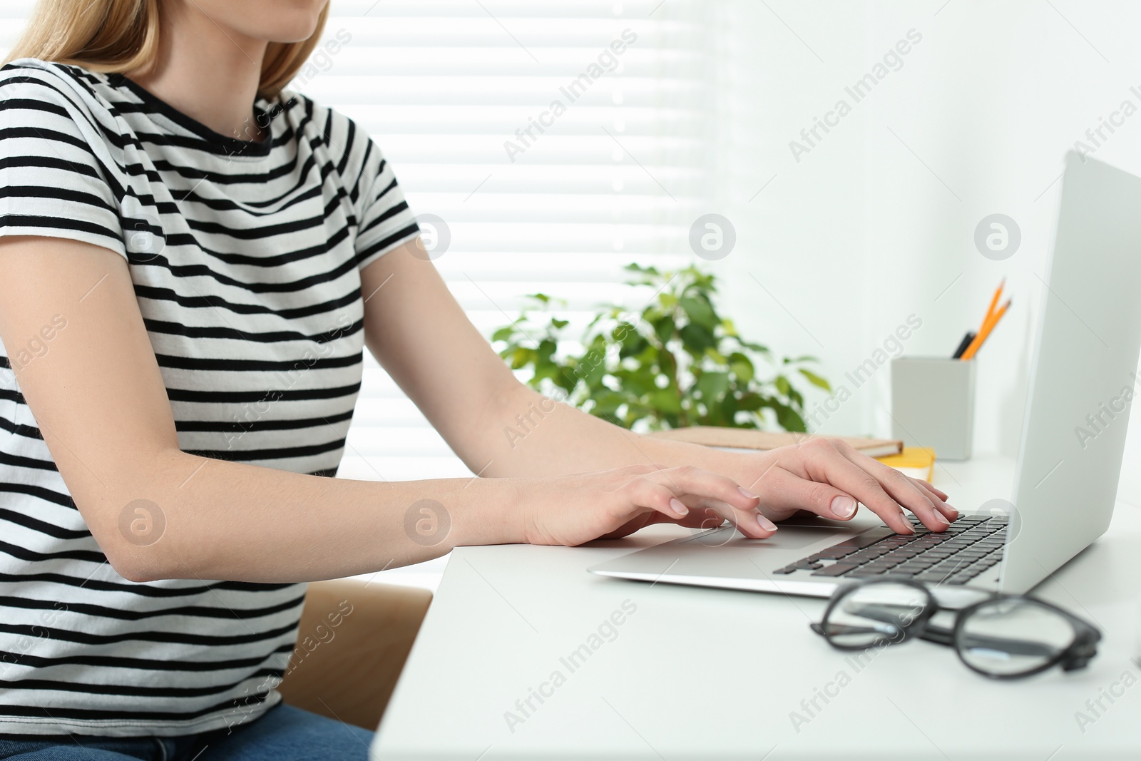 Photo of Home workplace. Woman typing on laptop at white desk indoors, closeup