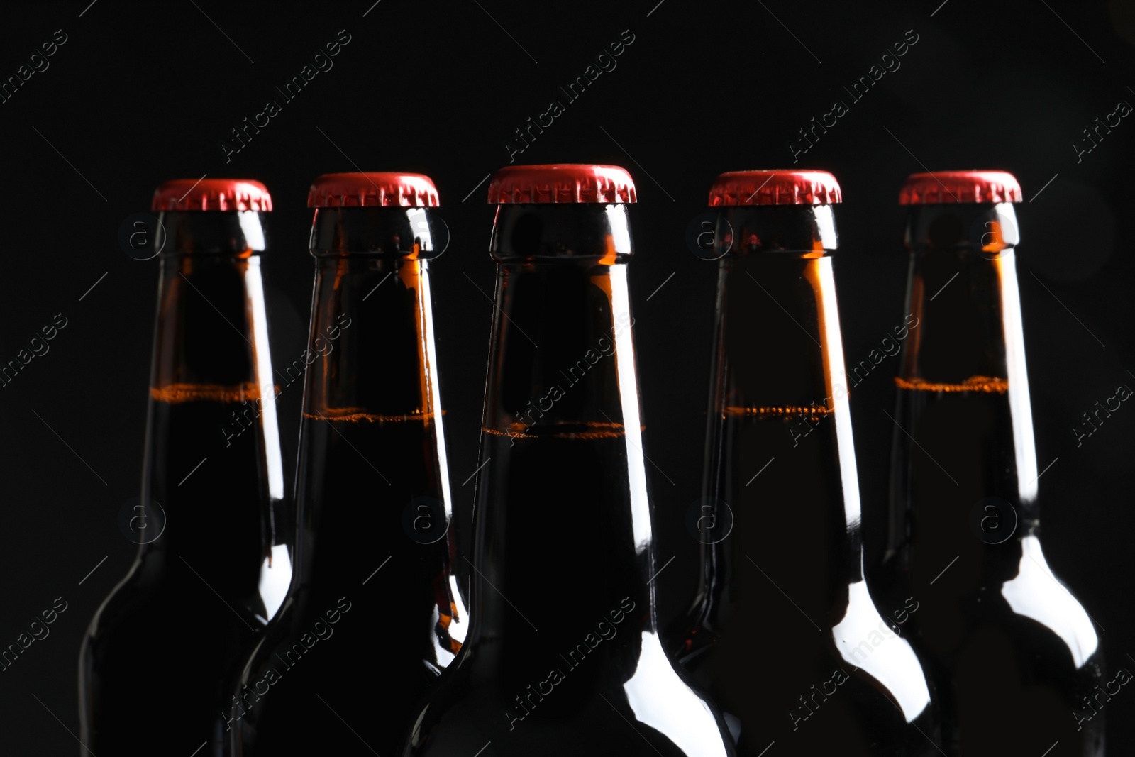 Photo of Bottles of tasty cold beer on black background, closeup