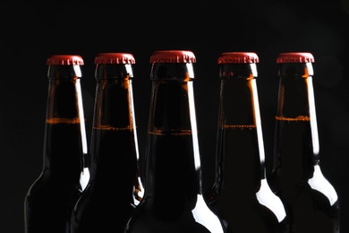 Photo of Bottles of tasty cold beer on black background, closeup