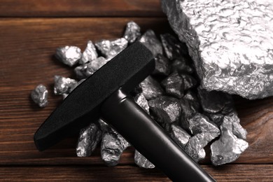 Photo of Pile of silver nuggets and hammer on wooden table, closeup
