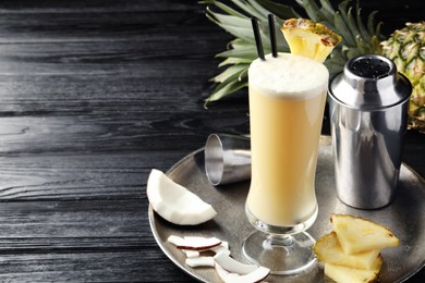 Photo of Tasty Pina Colada cocktail and ingredients on black wooden table, space for text