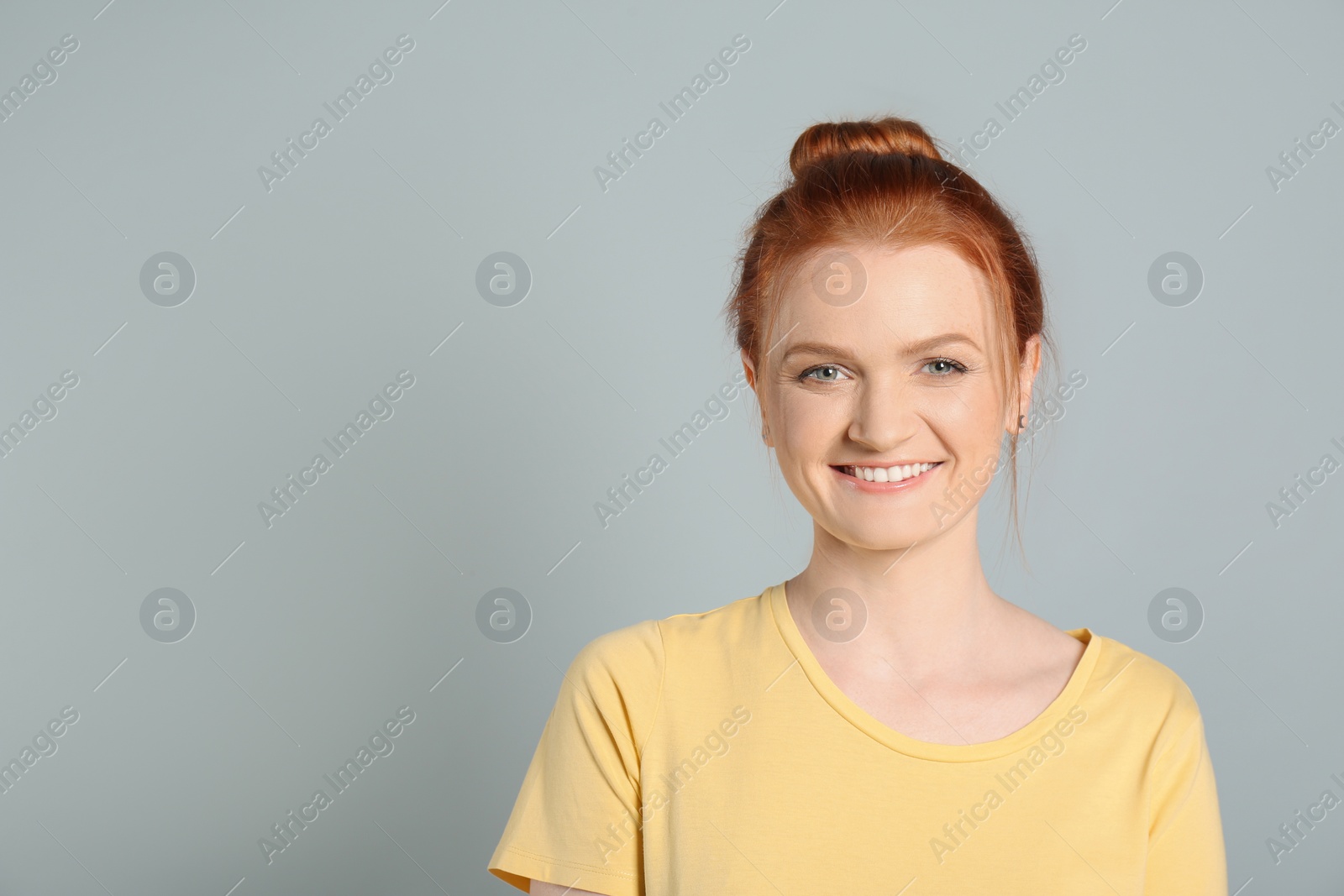 Photo of Candid portrait of happy red haired woman with charming smile on light grey background, space for text