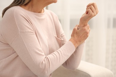 Mature woman suffering from pain in hand indoors, closeup. Rheumatism symptom