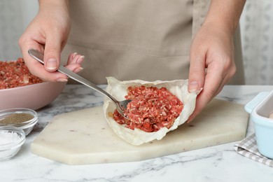 Photo of Woman preparing stuffed cabbage rolls at white marble table, closeup