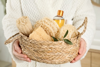 Photo of Woman holding wicker basket with natural loofah sponges in bathroom, closeup