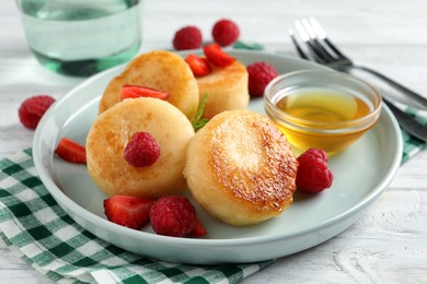 Photo of Delicious cottage cheese pancakes with fresh berries and honey on white wooden table, closeup