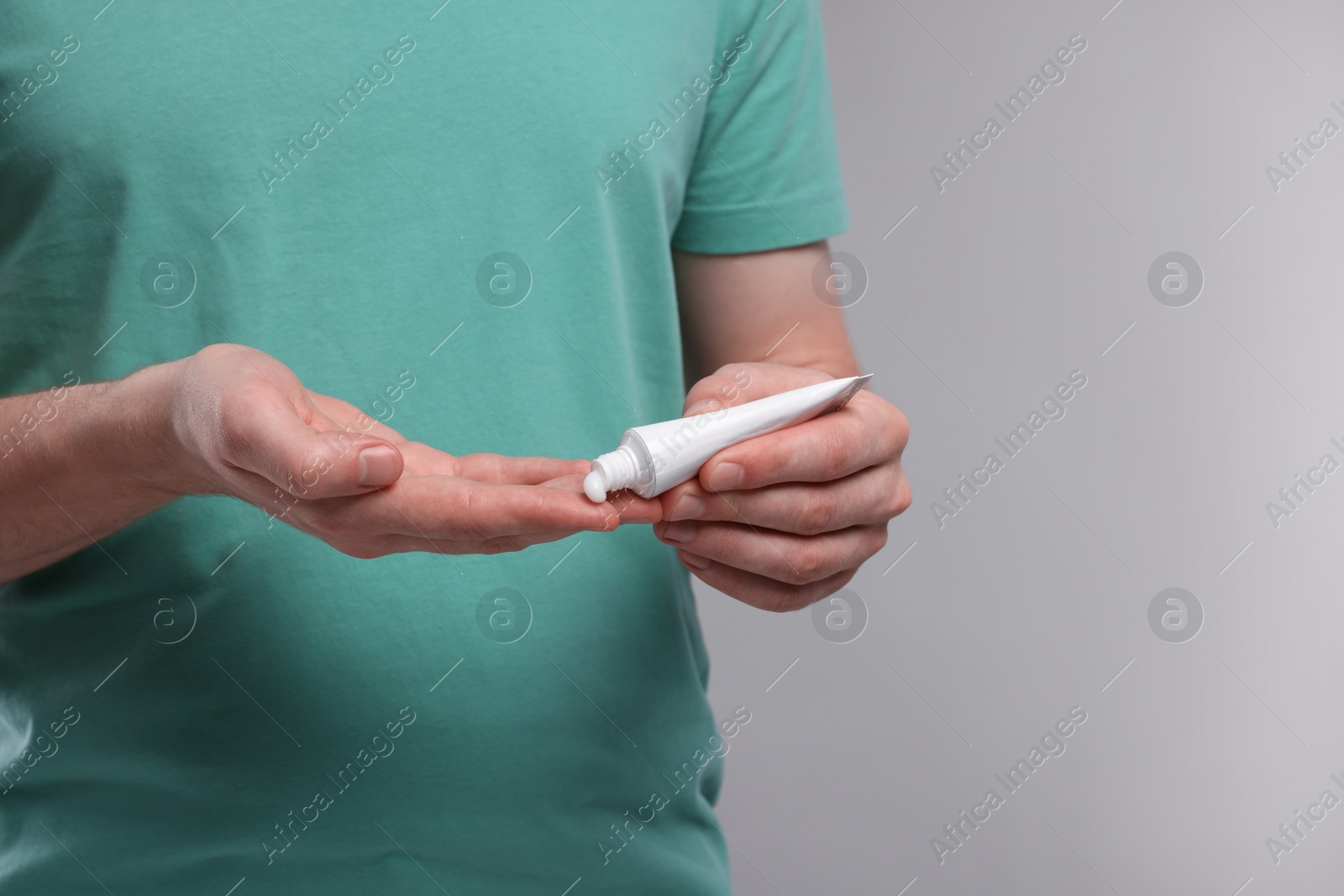 Photo of Man applying ointment from tube onto fingers on light grey background, closeup