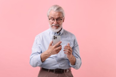 Portrait of stylish grandpa with glasses using smartphone on pink background