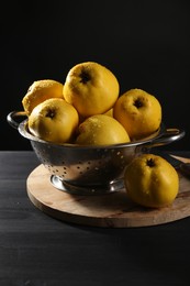 Photo of Tasty ripe quinces with water drops in metal colander on black wooden table