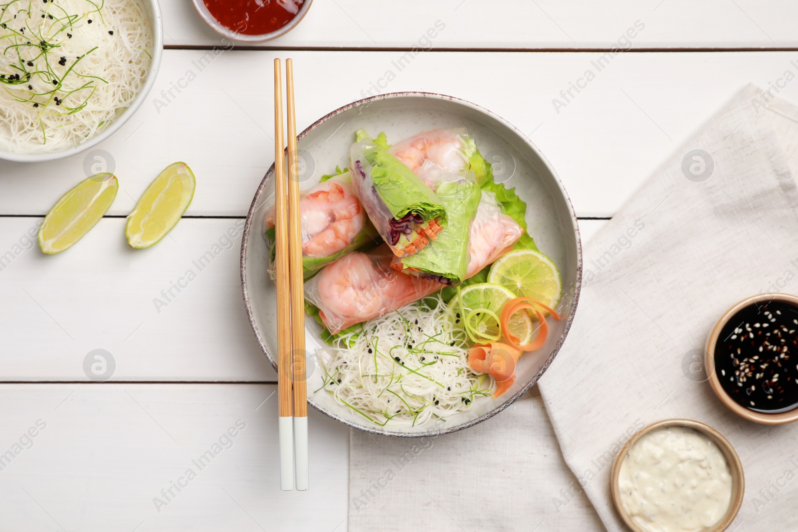 Photo of Delicious spring rolls wrapped in rice paper served on white wooden table, flat lay