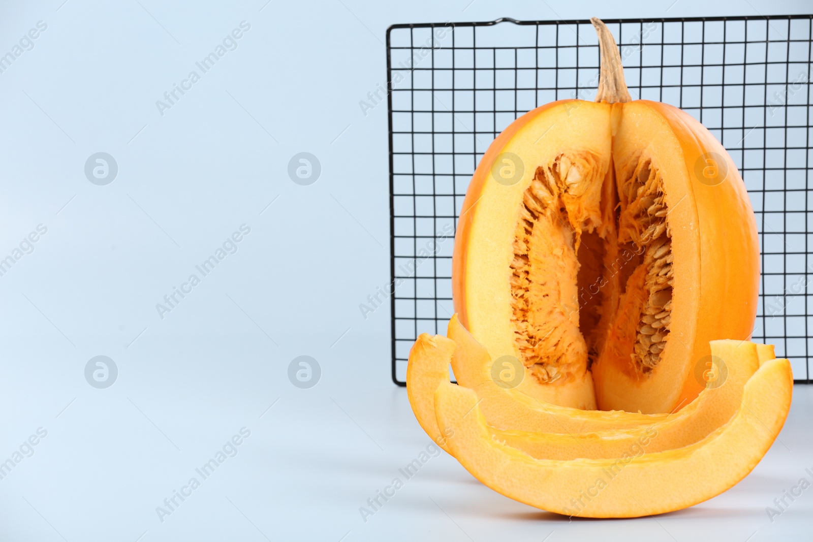 Photo of Cut fresh ripe pumpkin and cooling rack on light background, space for text