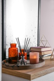 Photo of Wooden tray with air reed freshener and candles on table indoors