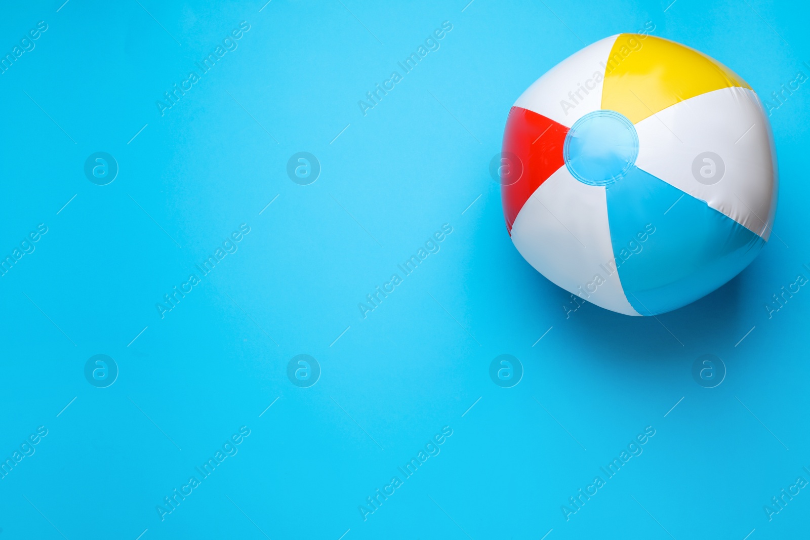 Photo of Bright beach ball on light blue background, top view. Space for text