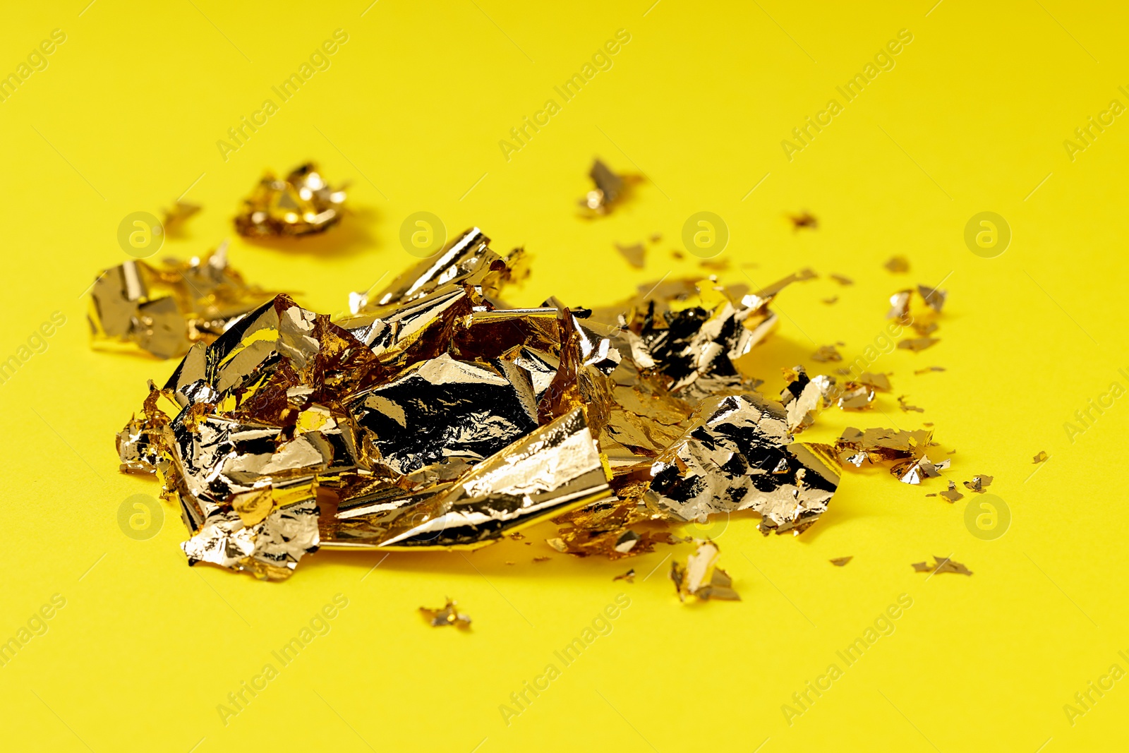 Photo of Many pieces of edible gold leaf on yellow background