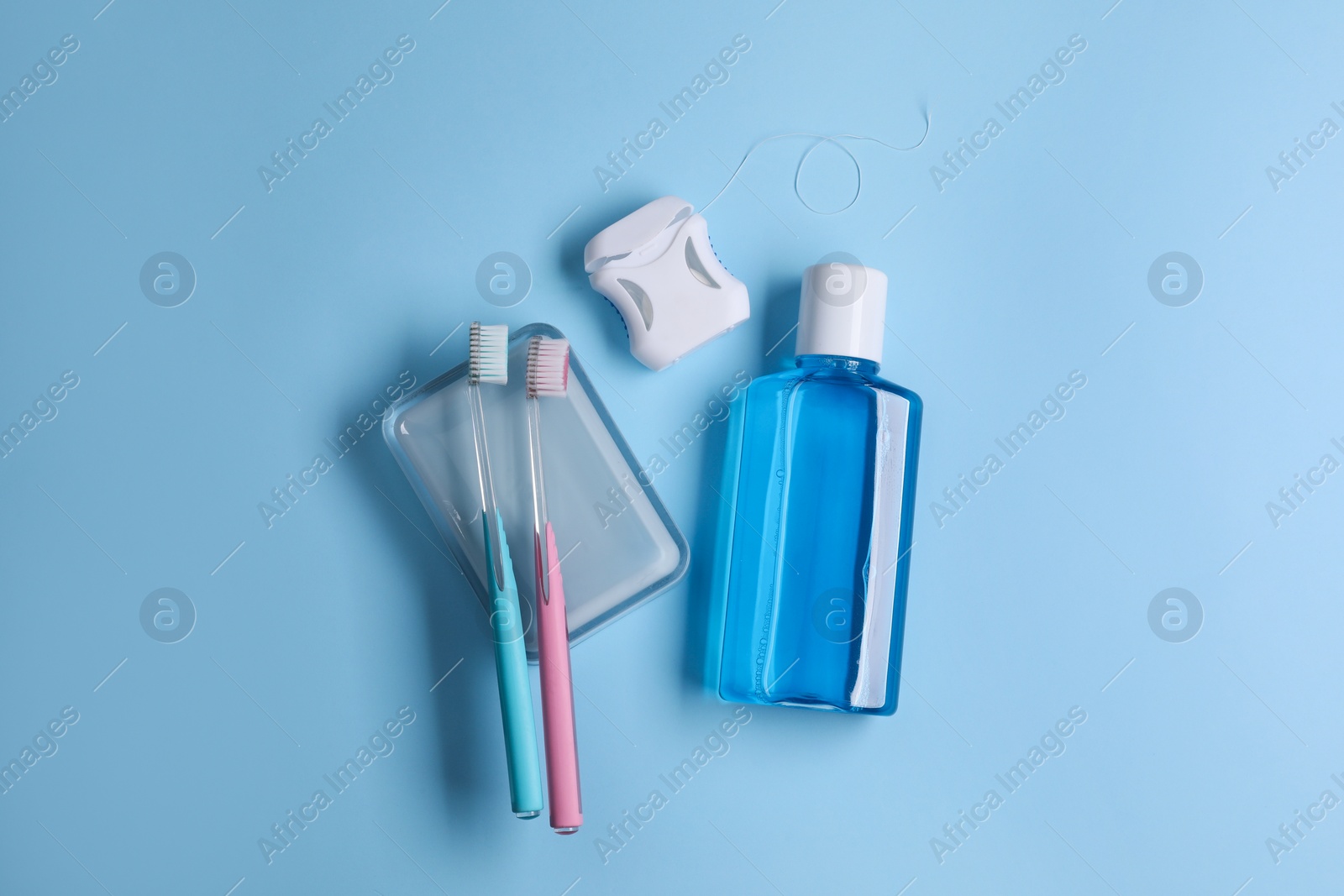 Photo of Fresh mouthwash in bottle, toothbrushes and dental floss on light blue background, flat lay
