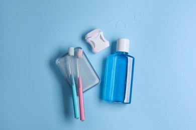 Photo of Fresh mouthwash in bottle, toothbrushes and dental floss on light blue background, flat lay