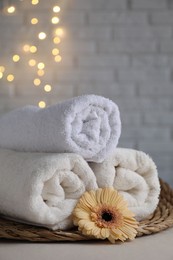 Rolled terry towels and flower on white table near brick wall indoors